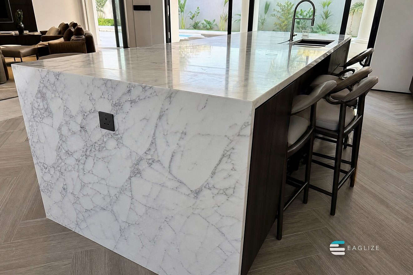 Kitchen island in stone with mitred waterfall ends, an inset sink and a bar overhang with stools